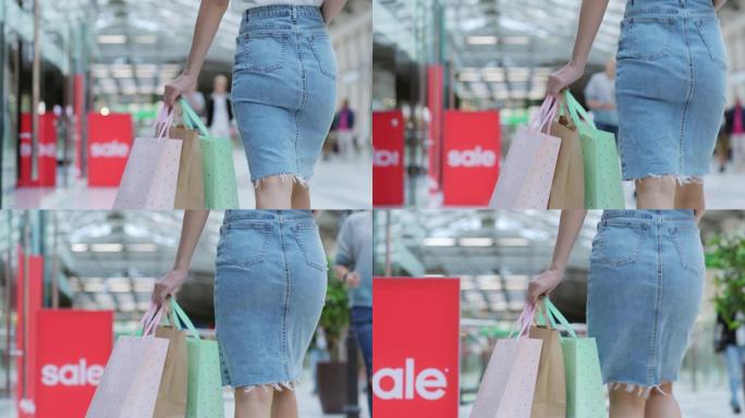 穿着牛仔铅笔裙的面目全非的女人手里拿着一堆购物袋走在购物中心