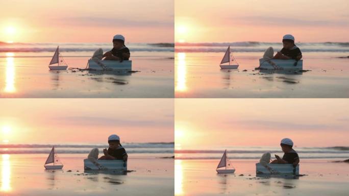 可爱的宝贝孩子，可爱的男孩，在海洋边缘的日落时玩船，泰迪熊和鱼，美丽的日落，倒影