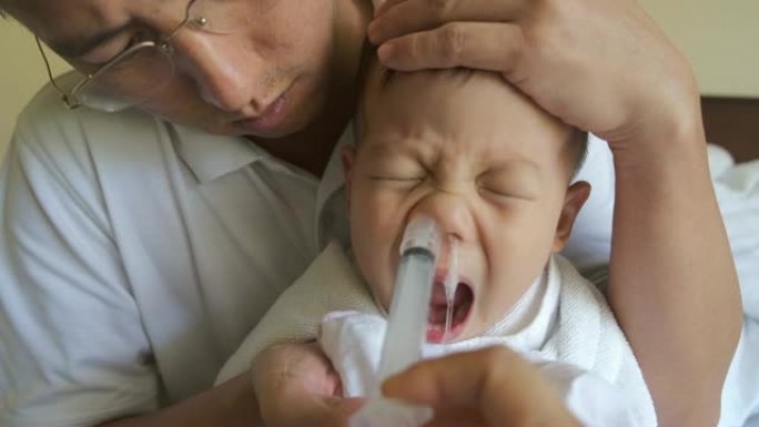 亚洲父母用注射器冲洗幼儿男童儿童鼻子，用于鼻腔冲洗