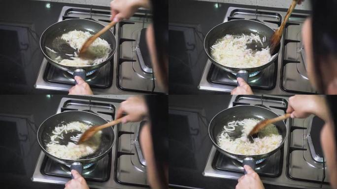女人的特写肩膀视图在家里的厨房的煤气炉上，在锅里用油煎炸洋葱片。烹饪食物。