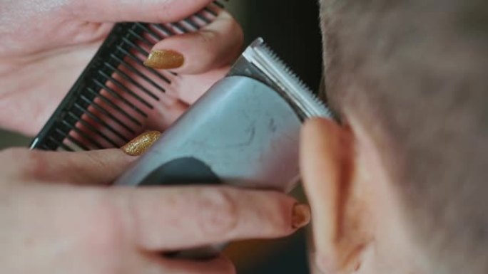 一个女美发师的手的特写镜头，用切发机制作一个头发边缘男孩。她给他做了一个现代发型。