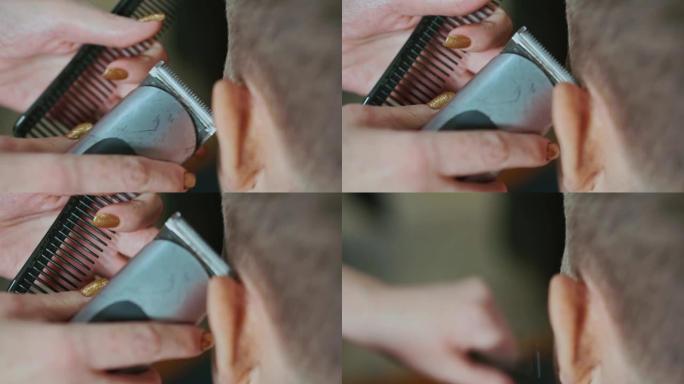 一个女美发师的手的特写镜头，用切发机制作一个头发边缘男孩。她给他做了一个现代发型。
