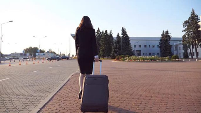 面目全非的女商人带着手提箱步行去机场出差。穿着高跟鞋的女士带着行李沿着城市街道行走。旅游概念。后视慢