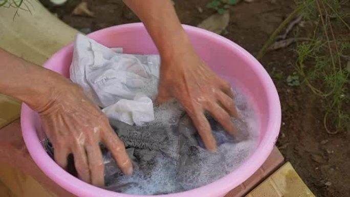 老妇人双手在粉红色的塑料碗中洗衣服