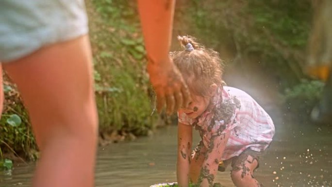 SLO MO的孩子在阳光明媚的森林里的小溪里玩泥