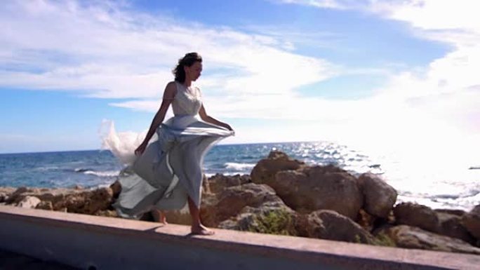 穿着裙子走在石滩上的优雅女人。夏季模特享受海洋景观