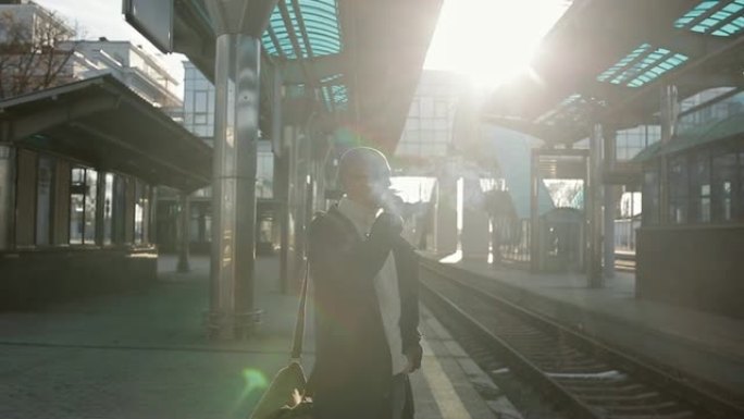 这位戴着眼镜的男子肩上扛着一个包，站在火车站的站台上等待晚点的火车。
