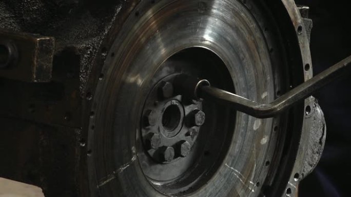 汽车发动机飞轮。机械师拧下钥匙飞轮。在车间里，从汽车发动机上拆下飞轮。