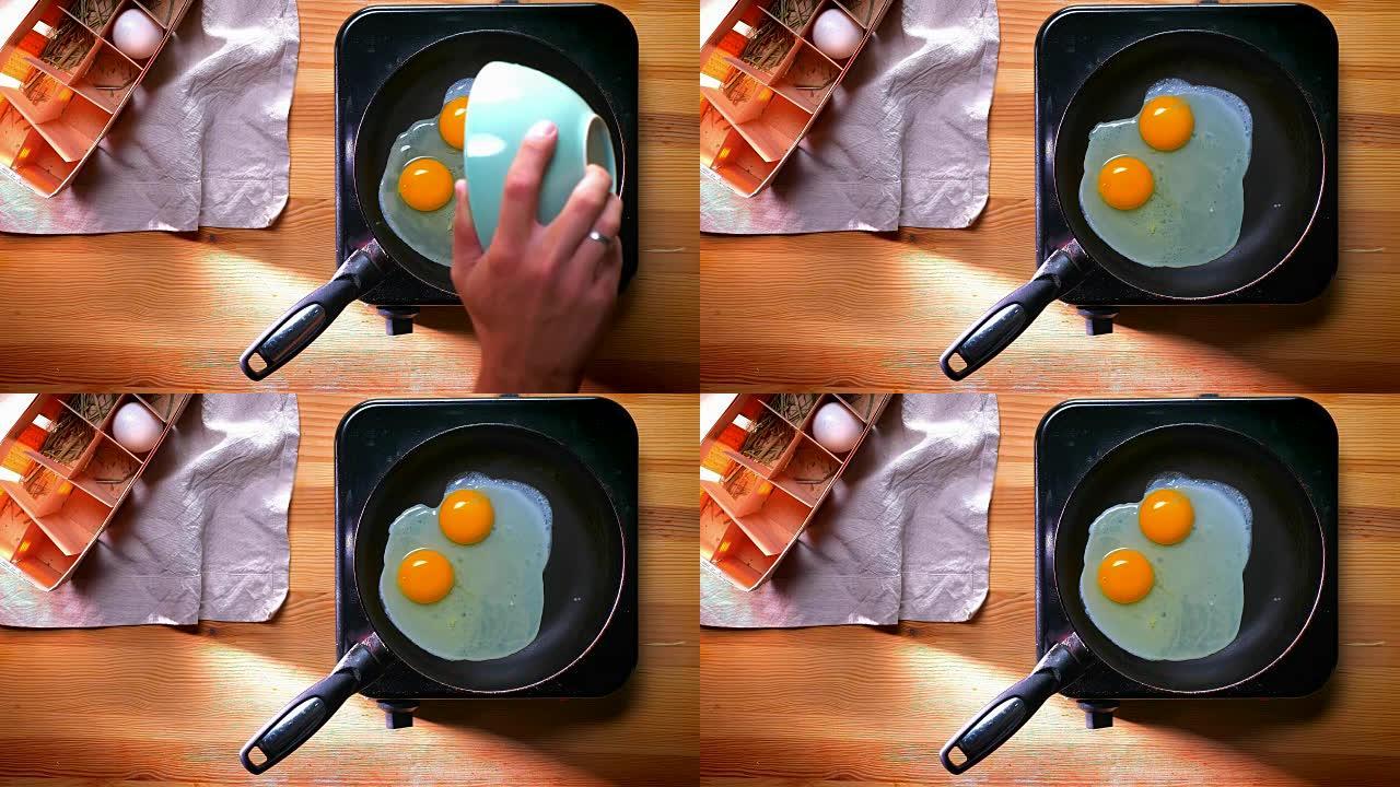 自上而下拍摄，两个有机鸡蛋在煎锅上准备早餐，并在阳光下在桌子上变白