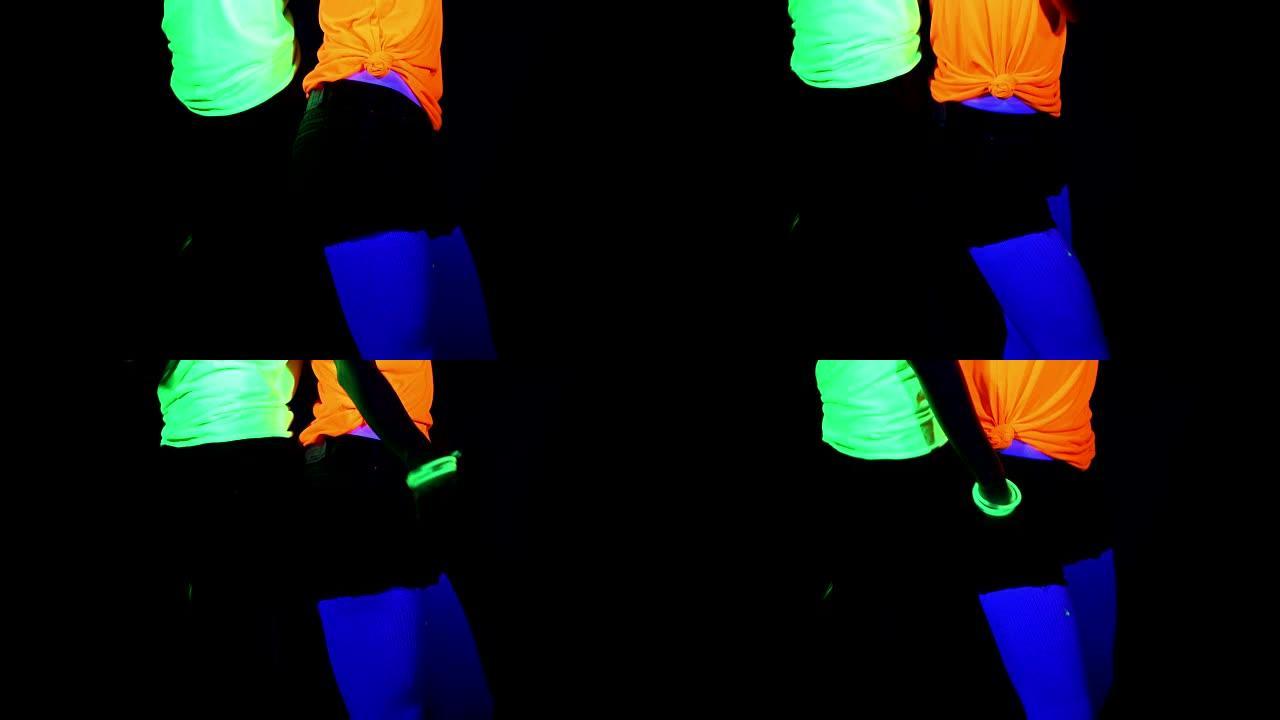 女人用紫外线的脸漆，发光的手镯，发光的眼镜，衣服在镜头前互相对着对方跳舞，中体拍摄。高加索人和亚洲女