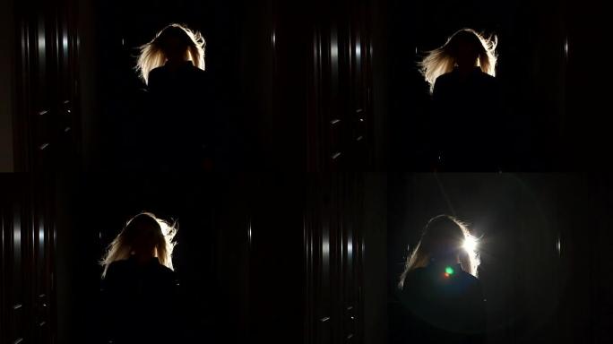 金发女孩的剪影在黑暗中的长长的走廊中，在风中飞舞