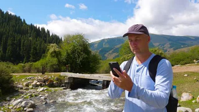 成年男子在石河景观山上徒步旅行时浏览手机