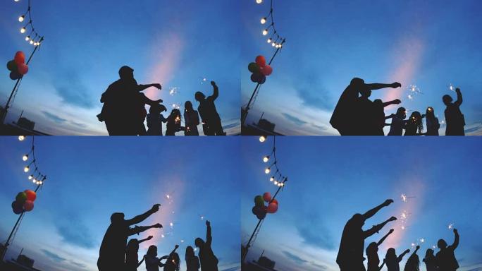 人们庆祝的剪影与朋友聚会一起在屋顶上放烟花，天空充满戏剧性。节日、新年快乐和圣诞节的概念。4k分辨率