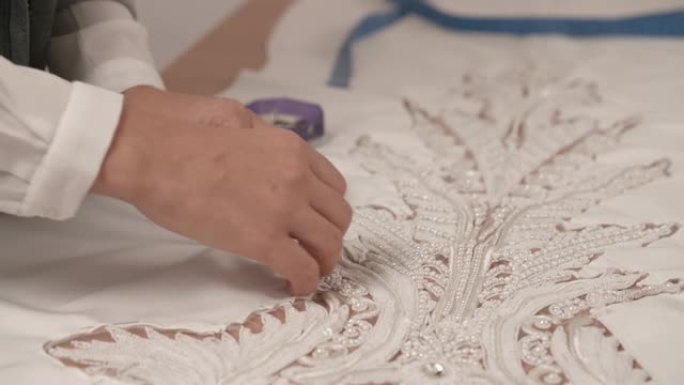 女性双手的特写镜头将花边钉在面纱上，以白色织物构成中心图案。婚纱的一部分。