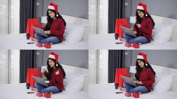 快乐的女人在网上购物，用电脑笔记本电脑和信用卡在床上买圣诞礼物