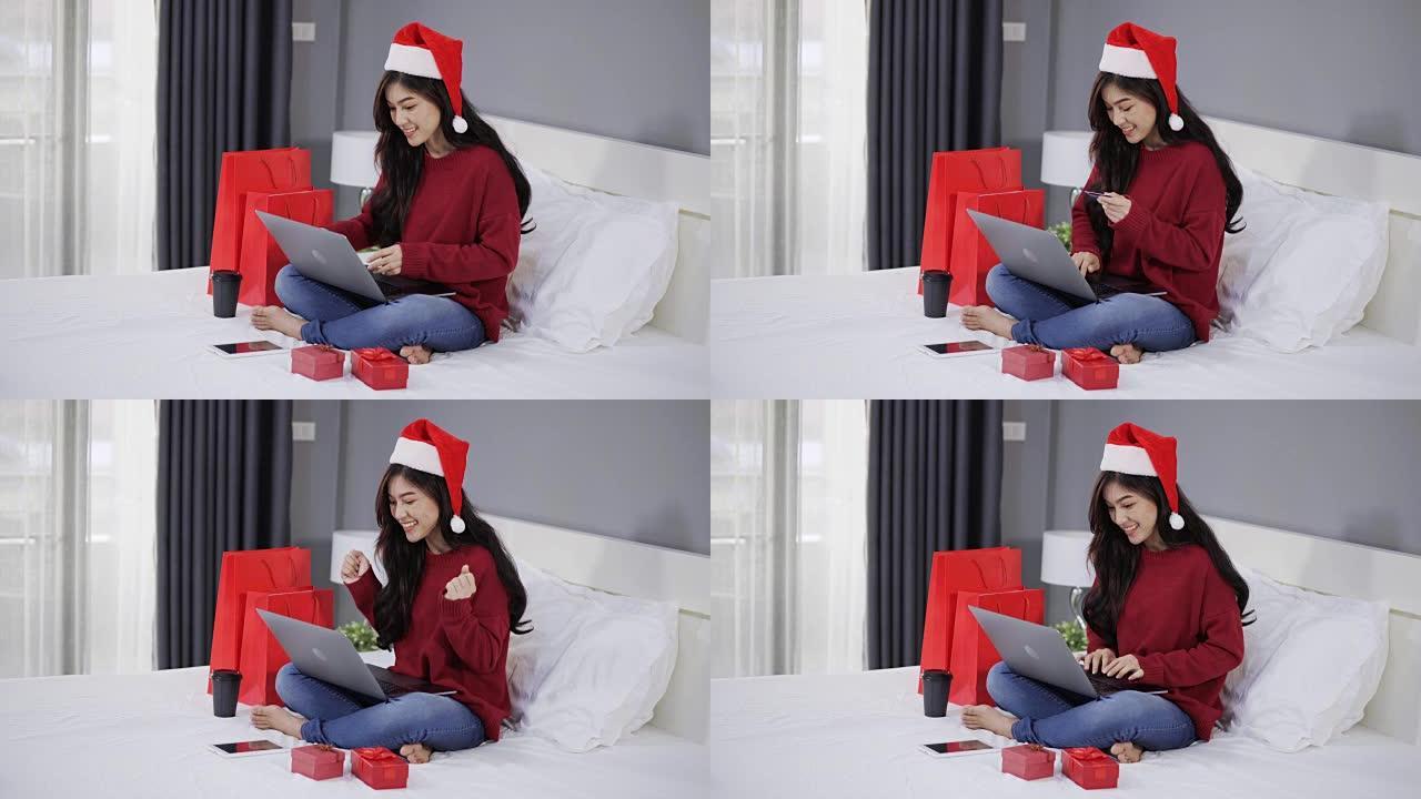 快乐的女人在网上购物，用电脑笔记本电脑和信用卡在床上买圣诞礼物