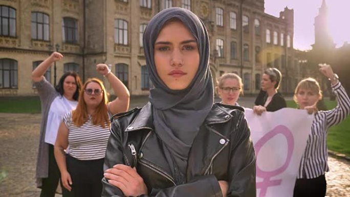 美丽的白人女性戴着头巾，双手交叉站在街上的女权主义者示威的中间