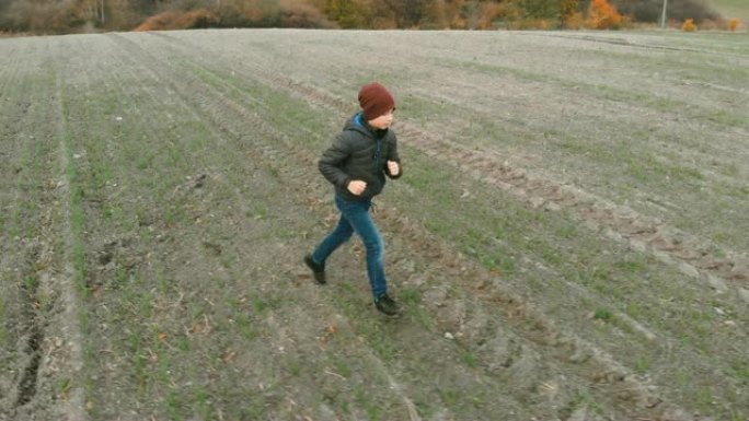 这个孤独的男孩在秋天在一片空旷，耕作的灰色田野中徘徊。黄花鱼正在野外寻找东西。这个男孩正在奔跑和行走