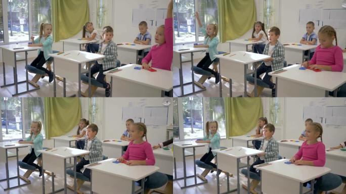 学校的孩子，男孩和女孩坐在课桌旁，在学校的教室里举手