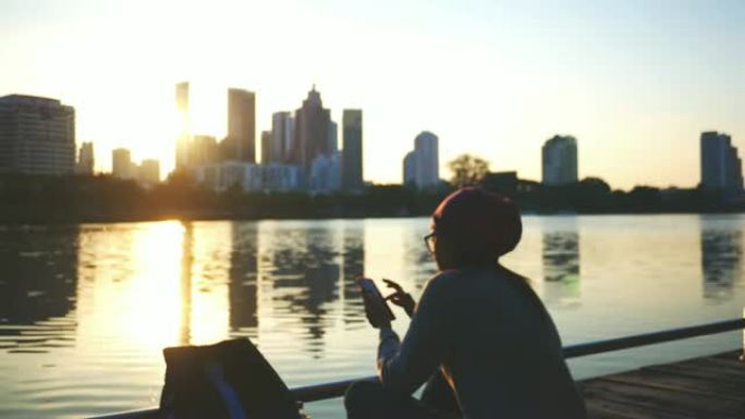 女游客在河边的码头上使用手机。背景模糊，作为首都的建筑物