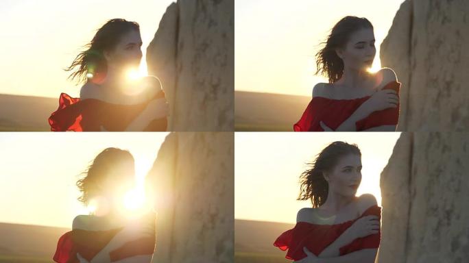 穿着红色连衣裙的年轻女子看着躲在悬崖后面的太阳风摇着她的头发