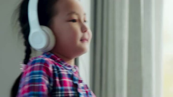戴着耳机的亚洲小女孩在家用智能手机跳舞