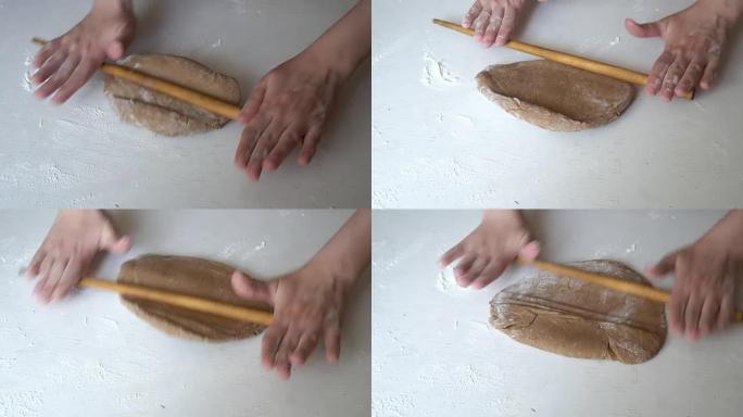 女人在白色的桌子上揉手棕色的面团，然后用木制的rolling面杖开始将其卷成煎饼。特写，高度细节。从