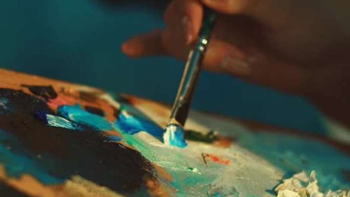 女艺术家用画笔在调色板上混合颜料。女人手握画笔