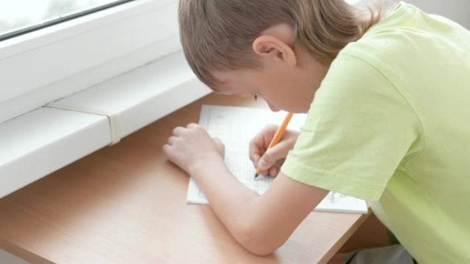 小学生男孩坐在桌子旁学习写信。做作业。