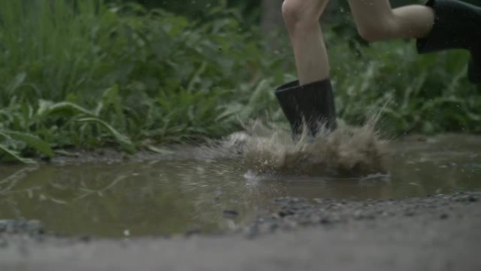 穿橡胶靴的男孩跳进水坑，男孩放纵，腿部特写，慢动作