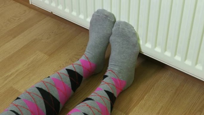 女人在暖气片前穿着彩色袜子保持冷脚