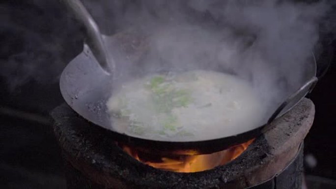 一个男人用炭炉做饭的慢动作镜头。用明火做的炒锅面条。泰国曼谷唐人街的街头美食
