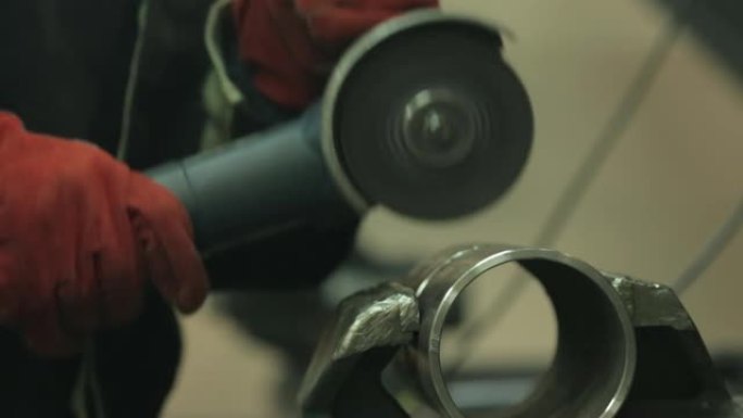 一位戴着红色手套的锁匠借助金属车间的研磨机清洁一段钢管上的焊缝