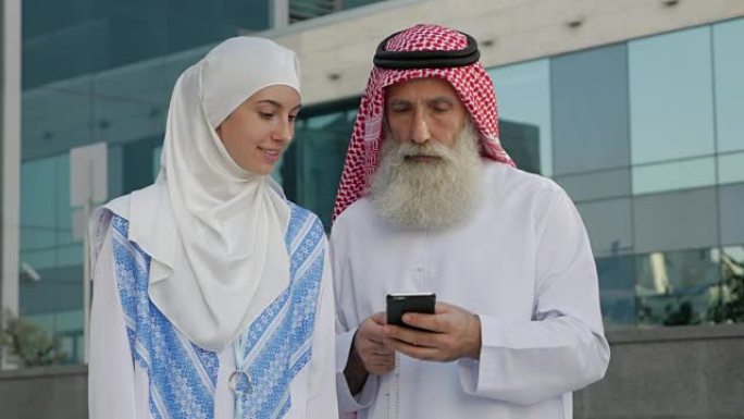 一个留着胡子的阿拉伯老年男子和一个年轻女孩在一个城市的智能手机上写一条信息