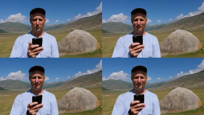 戴着帽子的男人的肖像浏览手机，后面有大石头和山