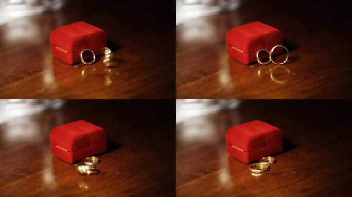 静态框架。两枚金戒指在红色表壳婚礼附近的木桌上旋转旋转