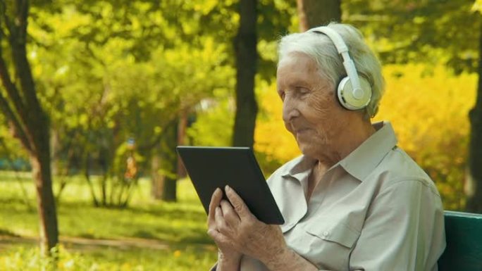 公园里有平板电脑和耳机的老人。视频通话。