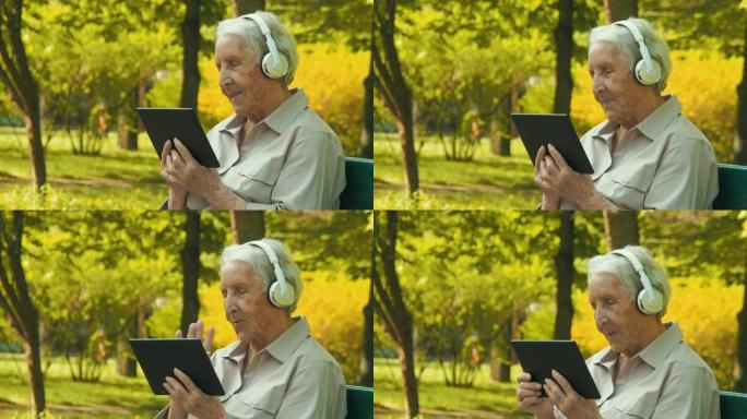 公园里有平板电脑和耳机的老人。视频通话。