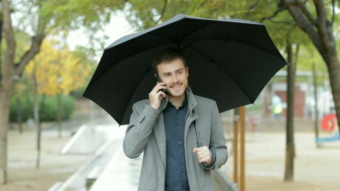 快乐的男人在雨中漫步在电话中