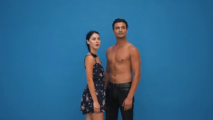 年轻美丽的西班牙裔夫妇在蓝墙前摆姿势。英俊的男人和女人
