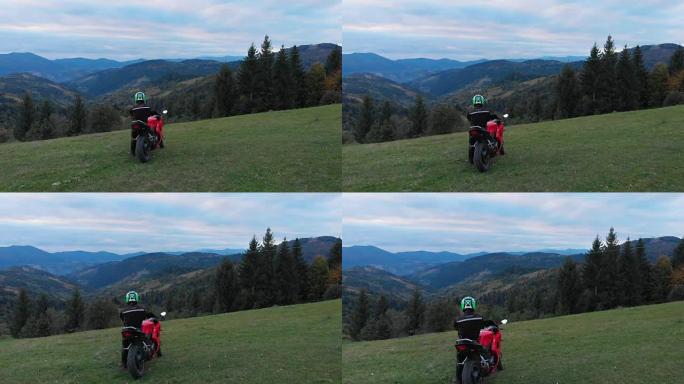 一个骑摩托车的人。年轻帅哥在山路上骑摩托车。那家伙站在他的摩托车旁边，看着群山。他很高兴。从四轴飞行