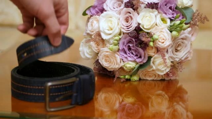 特写，美丽的婚礼花束玫瑰乳制品，白色和丁香。近处，男的手拿的是皮带。婚礼配件