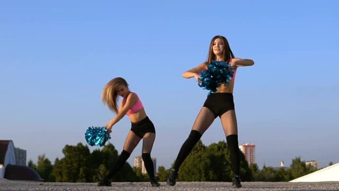 两个女孩啦啦队长着绒球在户外跳舞