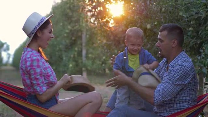 园丁家庭，年轻的妈妈和爸爸在阳光下的果园里与可爱的小孩玩草帽