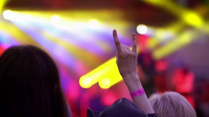夜间摇滚音乐会。人们欢呼雀跃，举起手来，在频闪的舞台灯光下齐声拍手。手部特写向上，显示摇滚标志。舞台