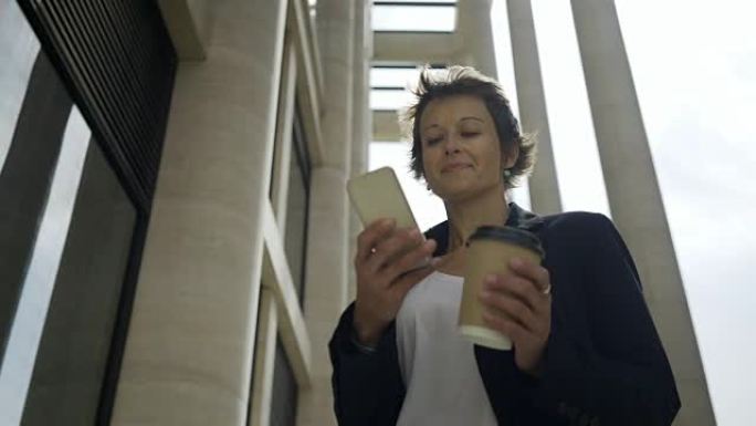中年女商人手持外卖咖啡杯的低角度平移镜头户外智能手机短信