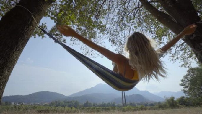 吊床上快乐的年轻女子在日落时摆动双腿，在大自然中尽情享受自由 -- 夏末。人们旅行快乐概念