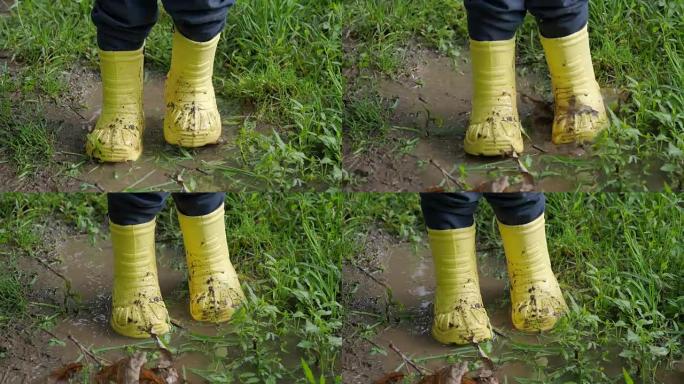 穿着亮黄色橡胶靴的小孩溅在水坑里。孩子的脚免受脏水的侵害