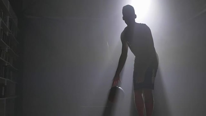 篮球运动员运球和投掷球，在背景为泛光灯的黑暗迷雾房间里打球