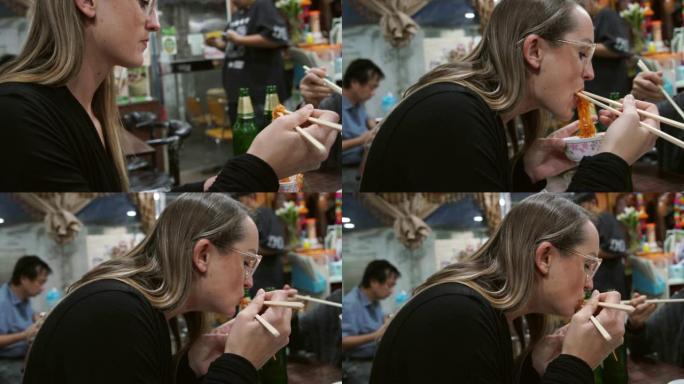 穿着眼镜的慢动作年轻女子在休闲餐厅享用筷子面条